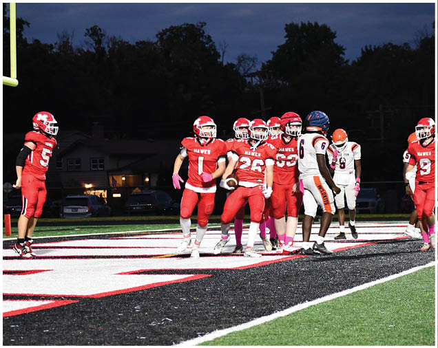 A group of people wearing red and white football uniforms are gathered on a field near the end zone during a nighttime game. Description generated by AI
