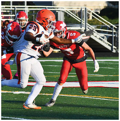 Three football players in red uniforms attempt to tackle a player in a white and orange uniform running with the ball on a green field. Description generated by AI