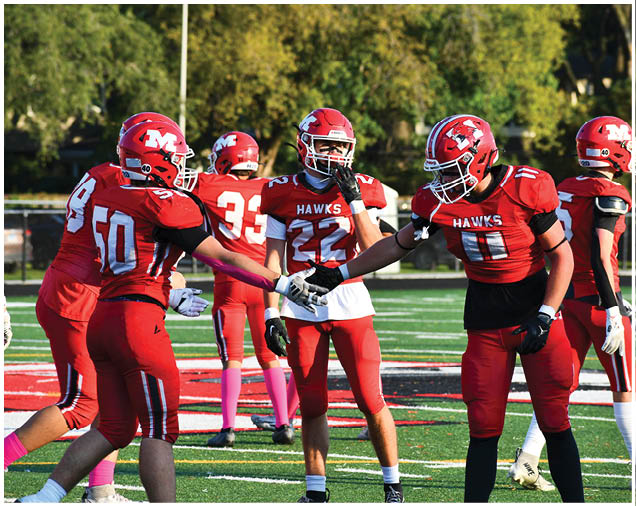 People in red football uniforms with helmets are on a field, with two players in the foreground giving a handshake. Description generated by AI