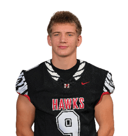 A person wearing a black football jersey with the number 9 and the word “HAWKS" stands with hands behind their back against a black background. Description generated by AI