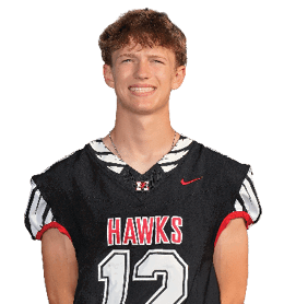 A person with short curly hair is smiling and wearing a black sports jersey with red and white accents that says “HAWKS." Description generated by AI