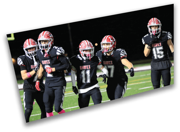 Five people in black football uniforms with red and white helmets are standing and walking on a football field at night. Description generated by AI