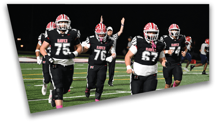 Adults in football uniforms with red and white helmets are running on a field during a nighttime game with a referee signaling in the background. Description generated by AI