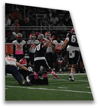 Players in football uniforms are actively engaged in a game on a field with spectators visible in the background. Description generated by AI
