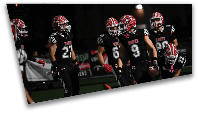 A group of people wearing black football uniforms with red and white helmets are gathered on a field at night, with one person holding a football. Description generated by AI