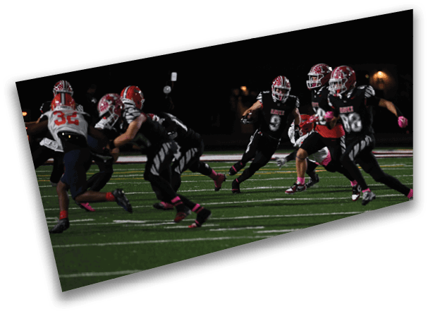 People wearing football uniforms are actively running on a field during a nighttime game. Description generated by AI