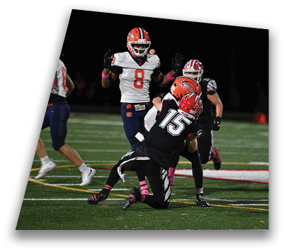 Two football players in black and orange uniforms are engaged in a tackle on a field while other players in white and orange uniforms look on. Description generated by AI