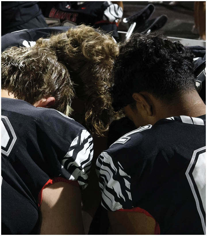 Two people wearing black sports jerseys with white and red accents are leaning their heads together in a close, supportive gesture. Description generated by AI