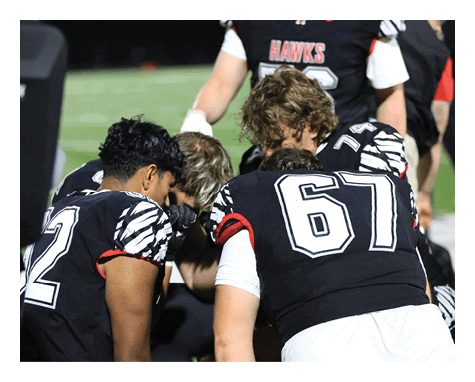 A group of people wearing black and white sports uniforms are huddled closely together on a field. Description generated by AI