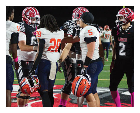 Several people wearing football uniforms and helmets are standing together on a field during a game. Description generated by AI