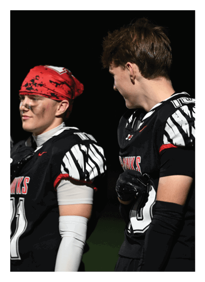 Two people wearing black and white football uniforms are standing and interacting with each other on a field at night. Description generated by AI