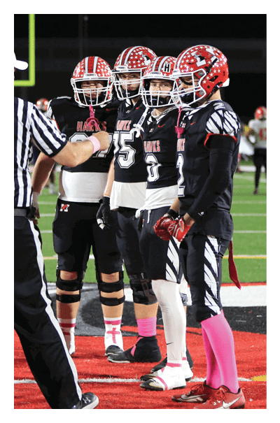 Several people wearing sports uniforms and striped referee shirts are standing on a football field near the center logo. Description generated by AI