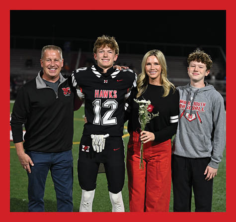 Four people stand on a football field at night with one person in a football uniform holding a flower and smiling. Description generated by AI