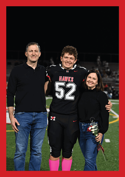 Three people stand closely together on a sports field at night, with one person embracing another while a third person looks on. Description generated by AI