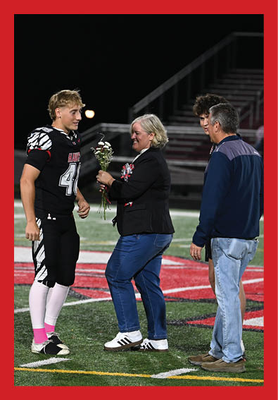 A person in a football uniform is receiving flowers from another person while two others stand nearby on a football field at night. Description generated by AI