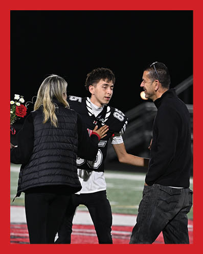 A person in a sports uniform is interacting with two people on a field, one holding a bouquet of flowers, during a nighttime event. Description generated by AI