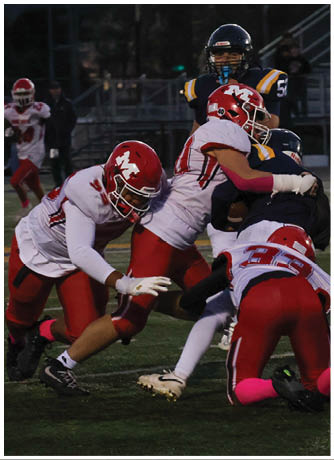 Several people wearing football uniforms are engaged in a tackle during a game on a grassy field. Description generated by AI
