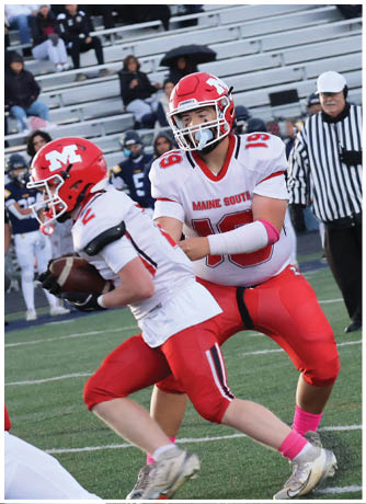 Two football players in red and white uniforms are engaged in a play on a field with a referee and spectators in the background. Description generated by AI