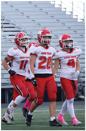 A person in a red and white football uniform with the number 55 is walking on a football field with empty bleachers in the background. Description generated by AI