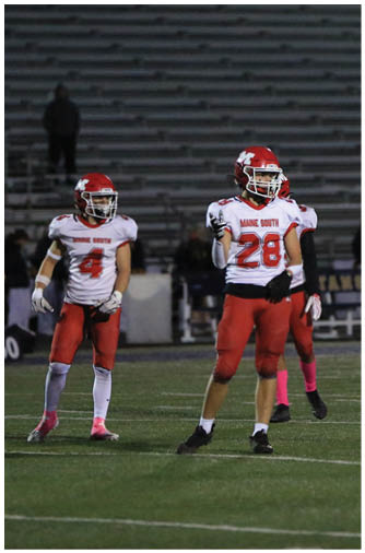 A person wearing a red and white football uniform with the number 28 stands on a football field at night with empty bleachers in the background. Description generated by AI
