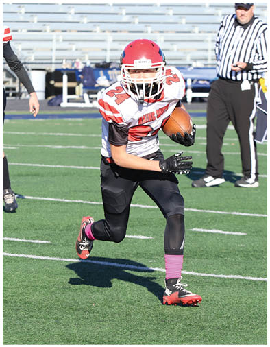 Two people in football uniforms are on a green field with one running and the other standing in the background. Description generated by AI