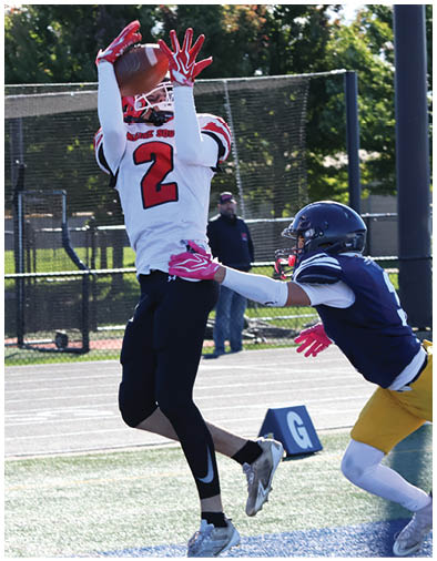 A person in a dark blue football uniform and helmet is reaching out to tackle or block another person wearing a white and red uniform during an outdoor football game. Description generated by AI