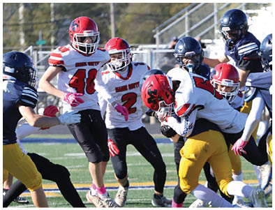A group of people wearing football uniforms are actively engaged in a game on a field with bleachers and spectators in the background. Description generated by AI
