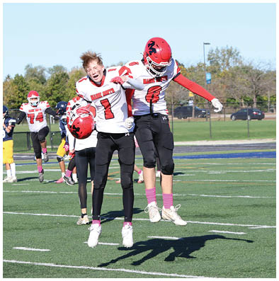 Two people in football uniforms jump and celebrate on a football field with others in the background. Description generated by AI