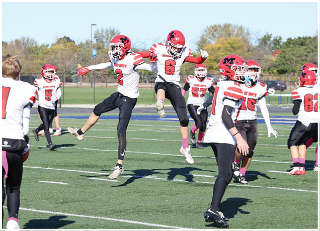 People in football uniforms with red helmets are warming up or practicing on a green field under a clear sky. Description generated by AI