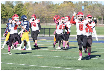 Children in football uniforms are playing on a field with one child in a white and red jersey raising a hand while running. Description generated by AI