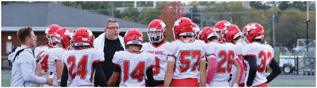 A group of people wearing red helmets and white sports uniforms are gathered around a coach who appears to be giving instructions on a sports field. Description generated by AI