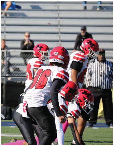 Several football players in red and white uniforms are on a field with two people sitting on bleachers in the background. Description generated by AI