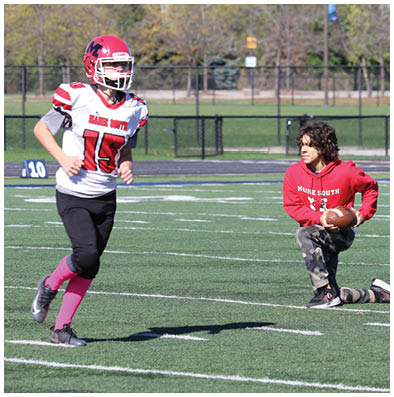 Several people wearing football helmets and uniforms are engaged in a tackle on a grassy field during a game. Description generated by AI