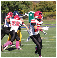 A person wearing a red football jersey with the number 18, black pants, and pink socks is standing on a green football field. Description generated by AI
