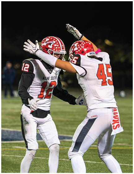 Two people wearing red and white football helmets and uniforms are celebrating with raised arms against a dark background. Description generated by AI
