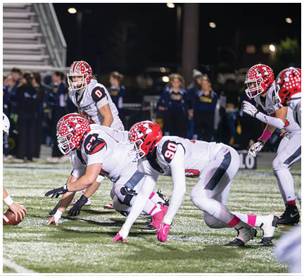 Two opposing American football teams are lined up at the line of scrimmage on a field during a night game with one team wearing white uniforms and the other wearing dark uniforms. Description generated by AI