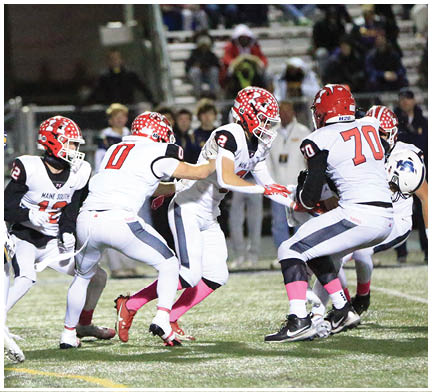 Several people in white and red football uniforms are actively engaged in a play on a football field with spectators in the background. Description generated by AI