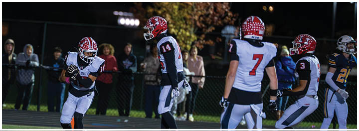Several people wearing football uniforms and helmets are on a field at night with spectators in the background. Description generated by AI