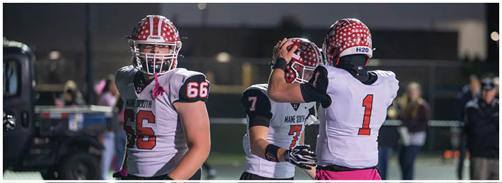 Three people in football uniforms are on a field with one person adjusting another's helmet while a third person stands nearby. Description generated by AI