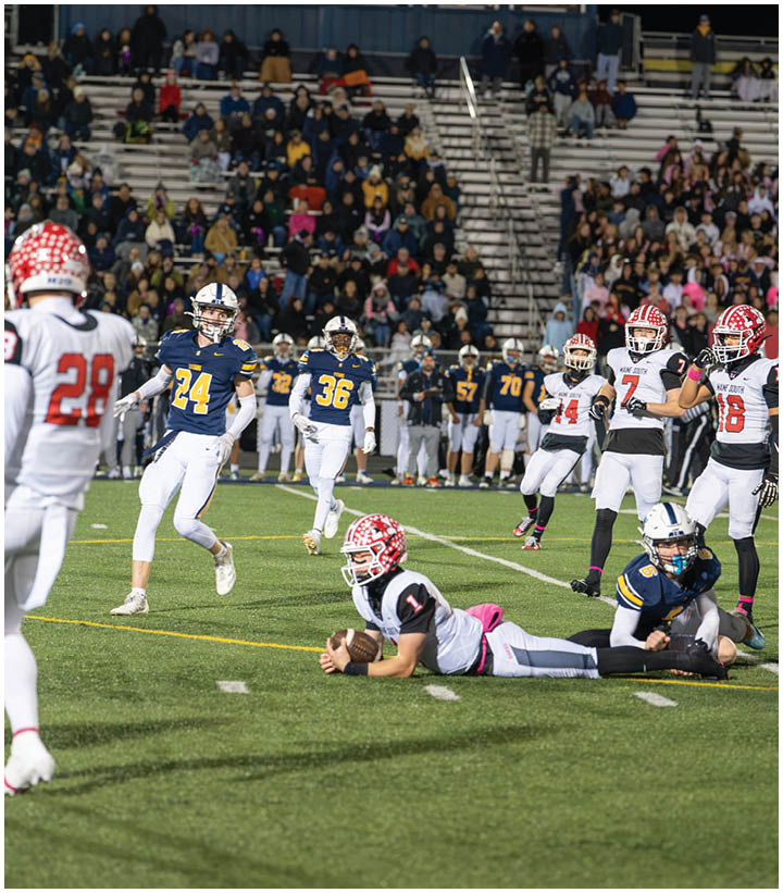 Two people wearing black and white football uniforms with red helmets are on a field at night, with one standing and the other kneeling. Description generated by AI