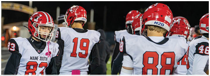 People wearing red helmets and white football jerseys with red numbers are standing on a football field at night. Description generated by AI
