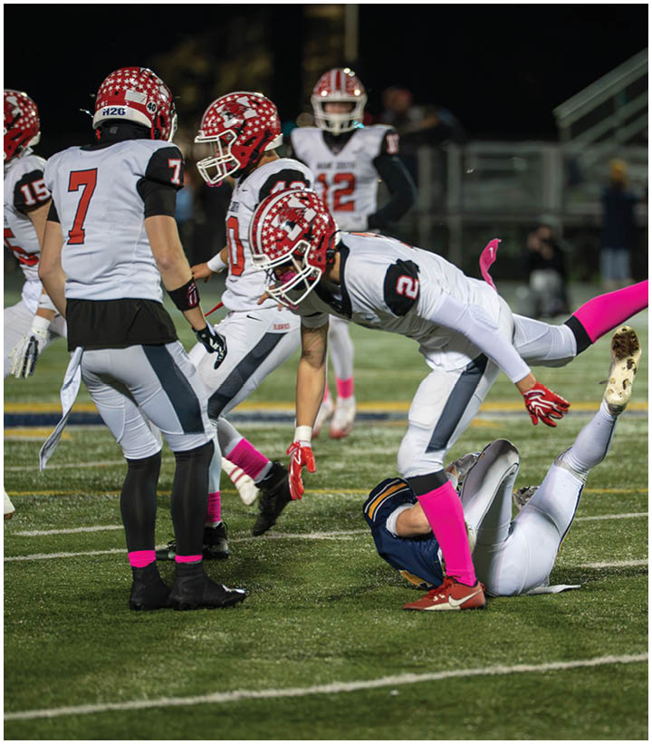 Several football players in white and red uniforms with pink socks are on a field at night, with one player falling over another player in a blue uniform lying on the ground. Description generated by AI