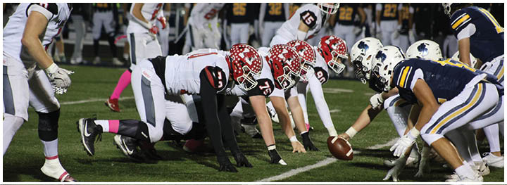 Two opposing American football teams are lined up at the line of scrimmage on a field, ready for the play to begin. Description generated by AI