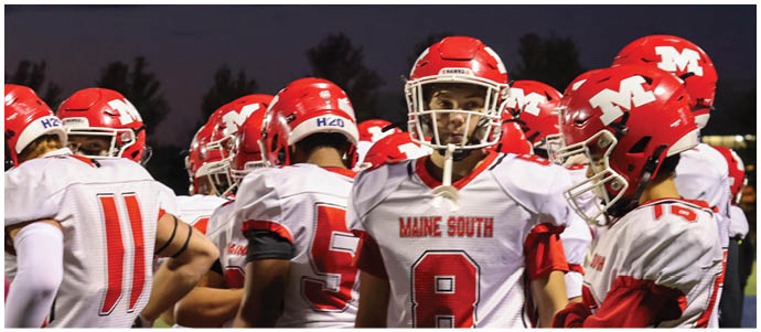 A group of people wearing white and red football uniforms with numbers and the text “Maine South" on the jerseys are standing closely together on a field. Description generated by AI