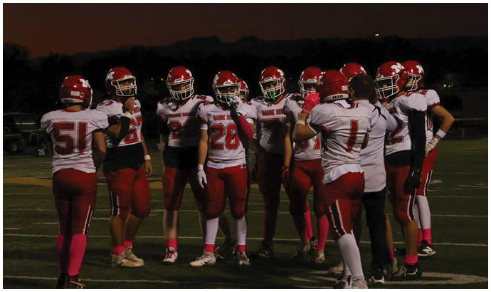 A group of people wearing football uniforms and helmets are gathered on a field under a dark sky. Description generated by AI
