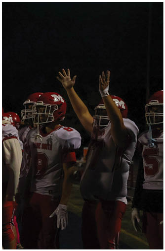 Two people in red football uniforms with pink socks are positioned on a football field facing opponents in white and orange uniforms during a game. Description generated by AI