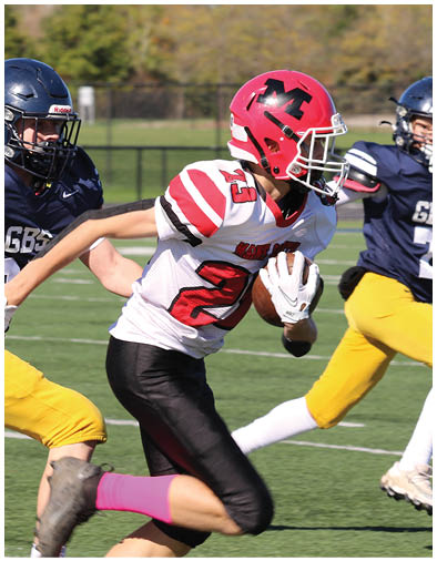 A person wearing a navy blue football uniform with yellow pants and a helmet is running on a grassy field while another person in a white and red uniform reaches out toward them. Description generated by AI