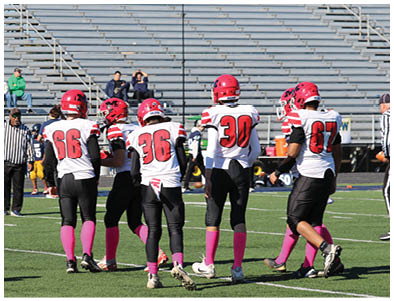 Five people in football uniforms with pink socks stand on a field while a referee walks nearby. Description generated by AI