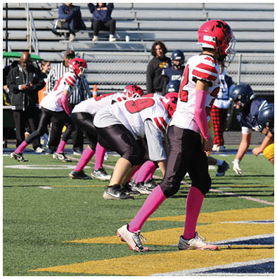 Adults in football uniforms from two teams are lined up on a field facing each other, preparing for a play during a game. Description generated by AI