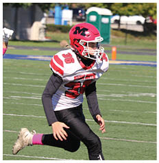 A person wearing a red helmet and white football jersey with the number 36 is running on a football field toward another person in a blue uniform. Description generated by AI